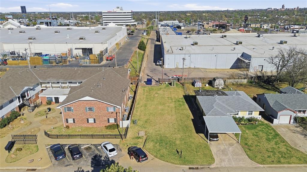 Aerial view of a grassy vacant lot between homes and large commercial buildings.