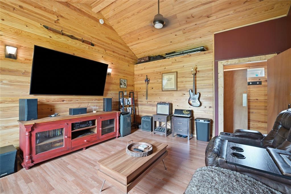 Wood-paneled living room with a vaulted ceiling, wall-mounted television, guitar, and leather seating.