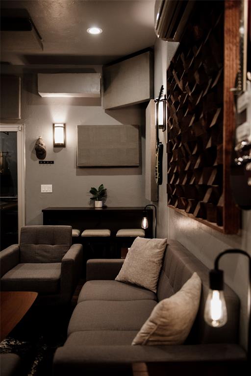 Living room with a gray sectional, armchair, warm pendant lights, and a wooden wall display rack.