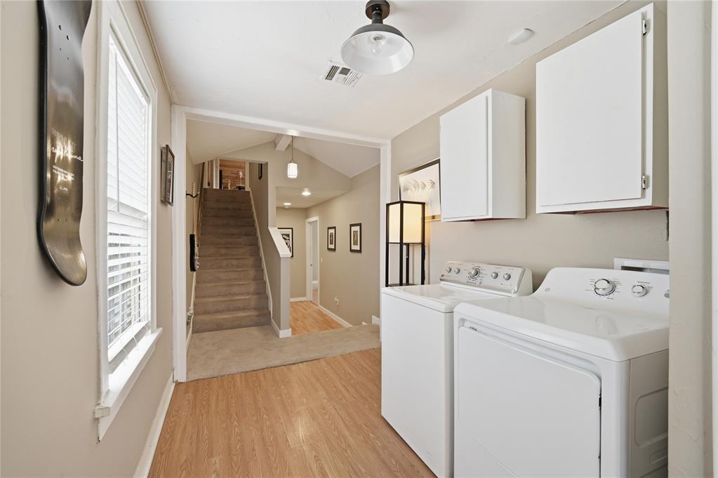 Laundry area with white washer and dryer, wall cabinets, and stairs beyond.