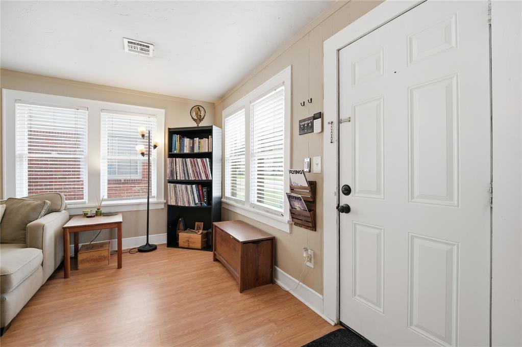 Furnished entry with a white paneled front door, window blinds, a bookshelf, and light wood flooring.