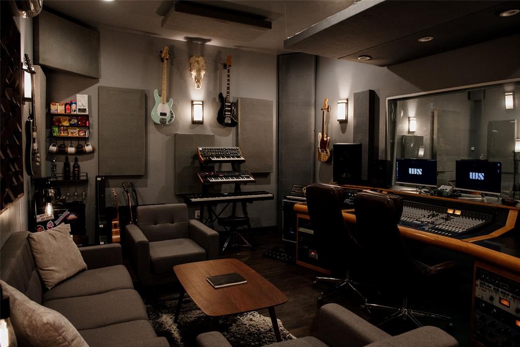 Recording studio with a mixing console, wall-mounted guitars, keyboards, and lounge seating.