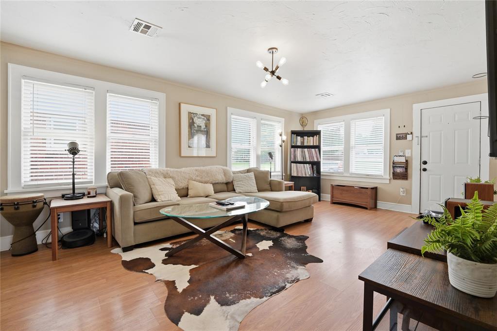 Living room with beige sectional, glass coffee table, cowhide rug, and bright windows.