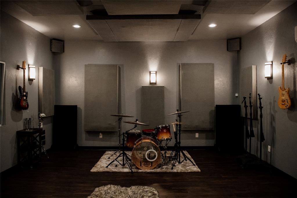 Music room with a drum kit on a rug, wall-mounted guitars, and acoustic panels.