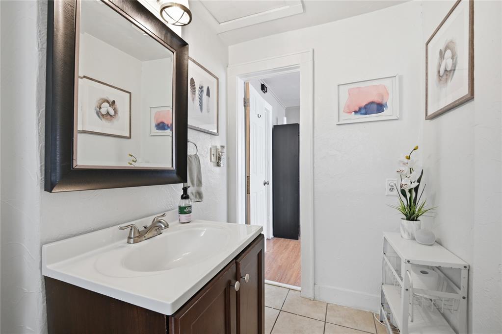 Bathroom with a dark wood vanity, white sink, large mirror, and tiled floor.