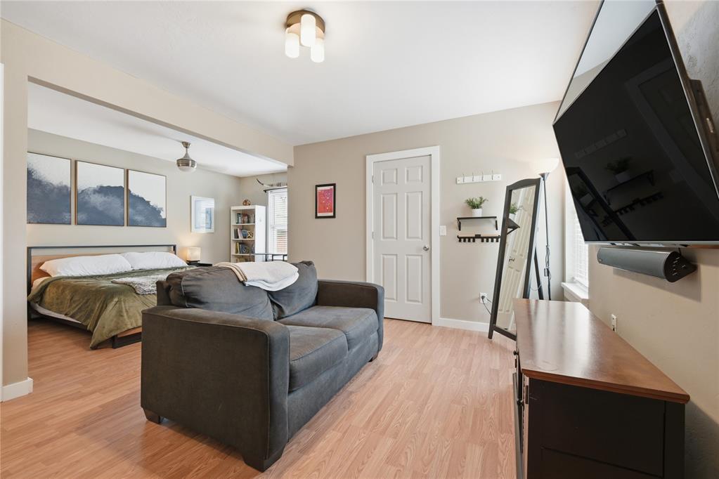 Bedroom with a bed, gray loveseat, light wood flooring, and wall-mounted television.