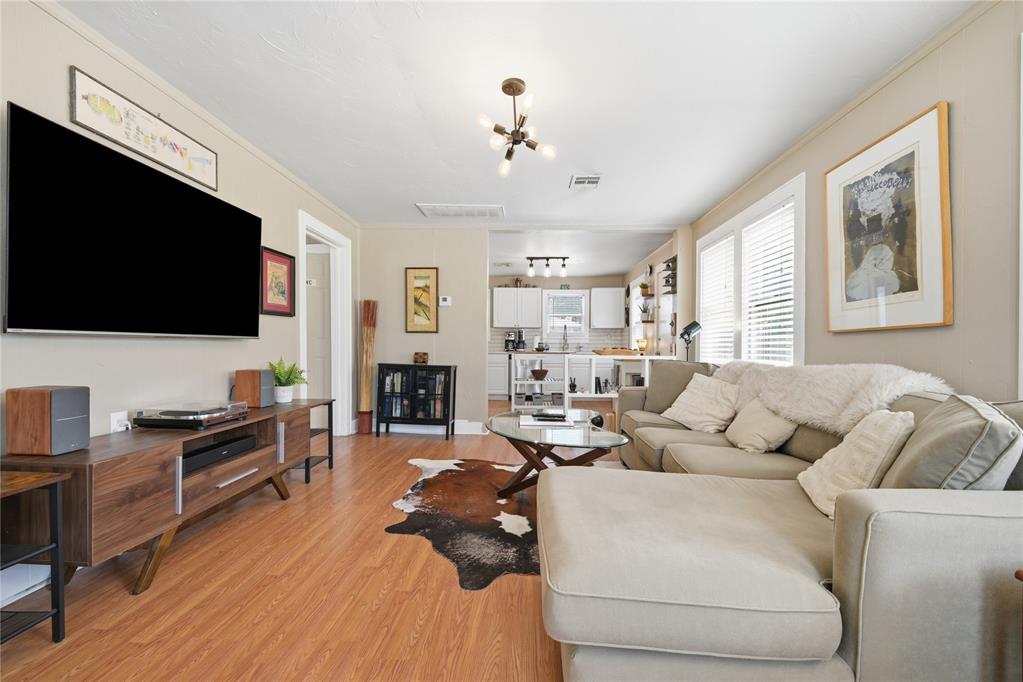 Furnished living room with a light sectional, wood floors, and an open kitchen beyond.