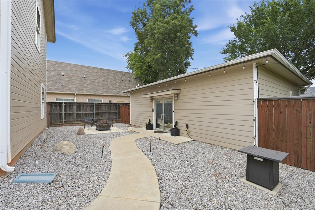Enclosed gravel courtyard with a curved walkway, patio seating, and a beige outbuilding.