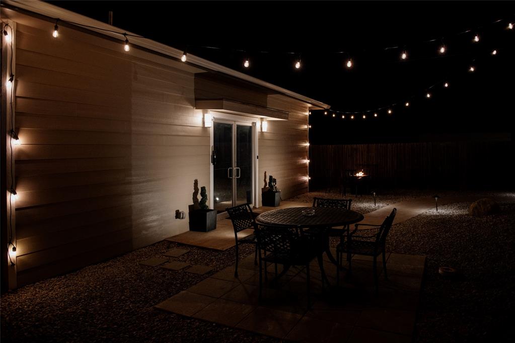 Patio dining set beside sliding glass doors, illuminated by warm string lights.
