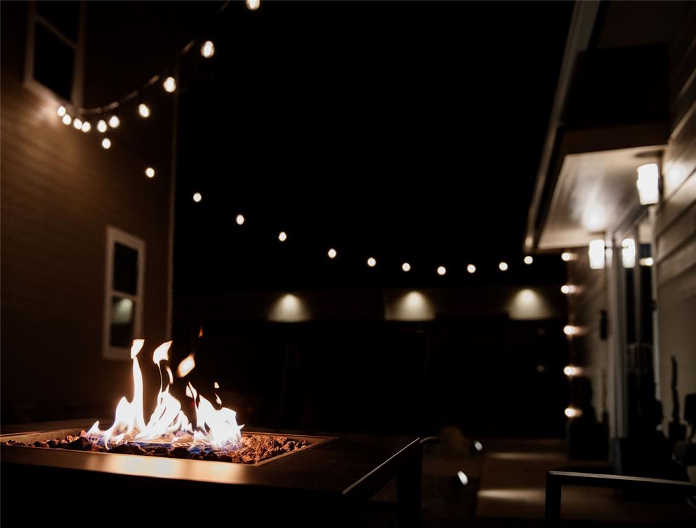 Outdoor patio with a glowing fire pit beneath string lights at night.