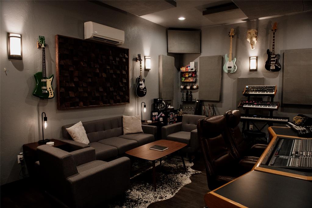 Music studio with wall-mounted guitars, keyboards, a mixing console, and a lounge seating area.