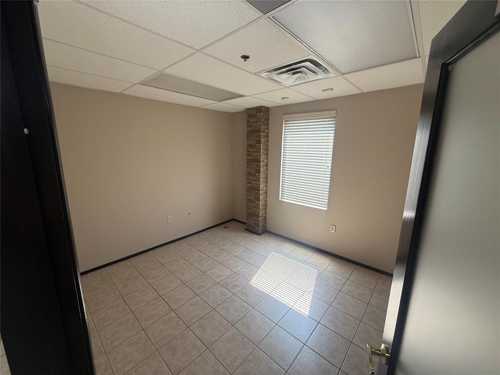 Vacant office room with tiled flooring, a brick column, and a window with blinds.