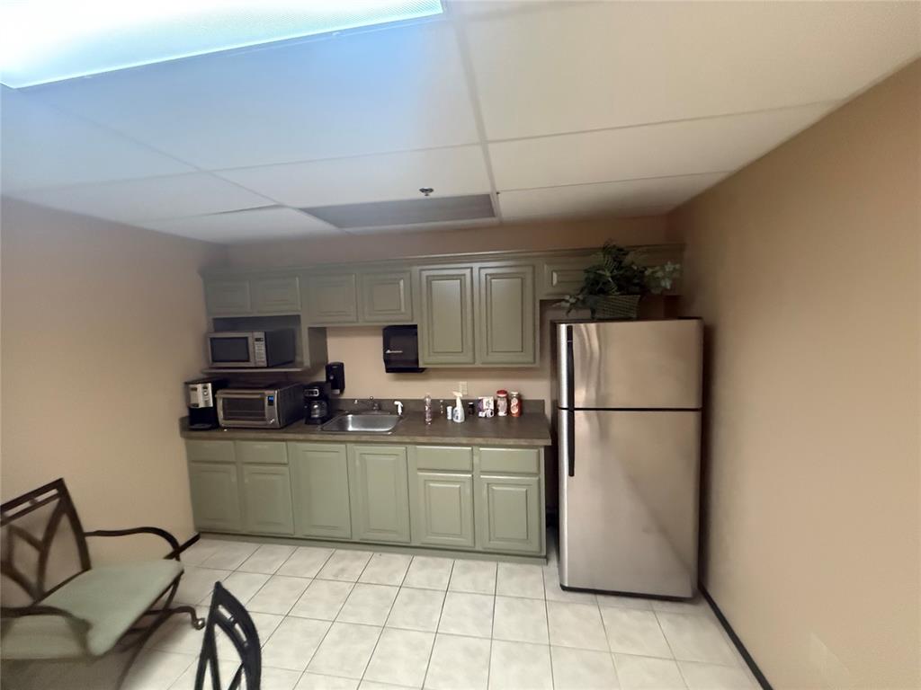 Kitchenette with pale green cabinets, countertop appliances, and a stainless steel refrigerator.