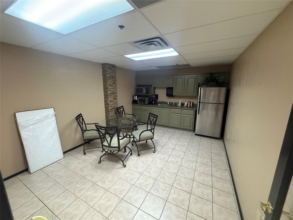 Commercial break room with green cabinets, stainless steel refrigerator, and glass dining table.