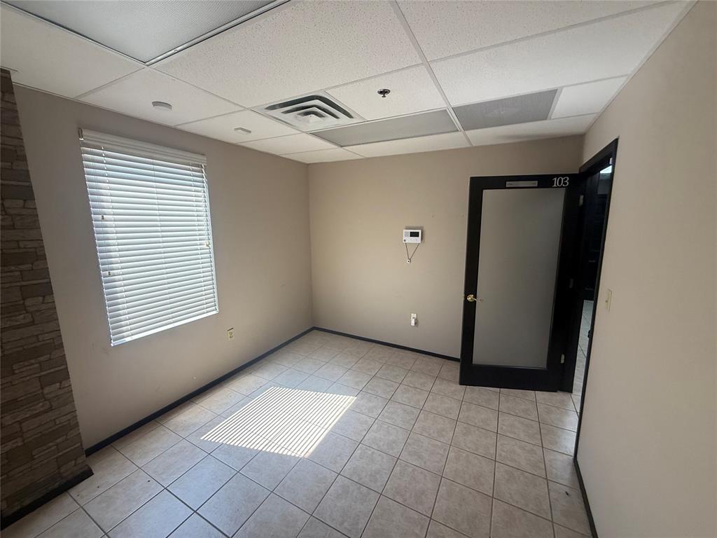 Empty office suite room with tiled floor, window blinds, stone accent wall, and open door marked 103.