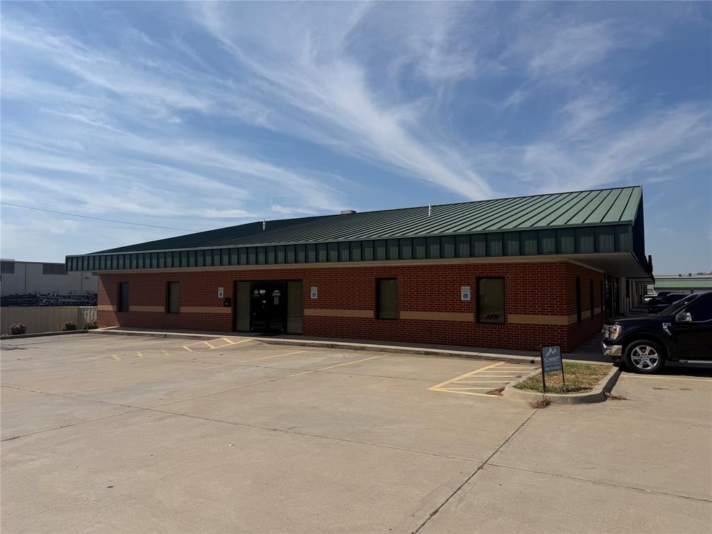 Commercial building with red brick walls, a green metal roof, and a concrete parking lot.