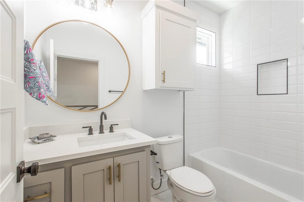 Bathroom with a white vanity, round brass-framed mirror, and white-tiled tub surround.