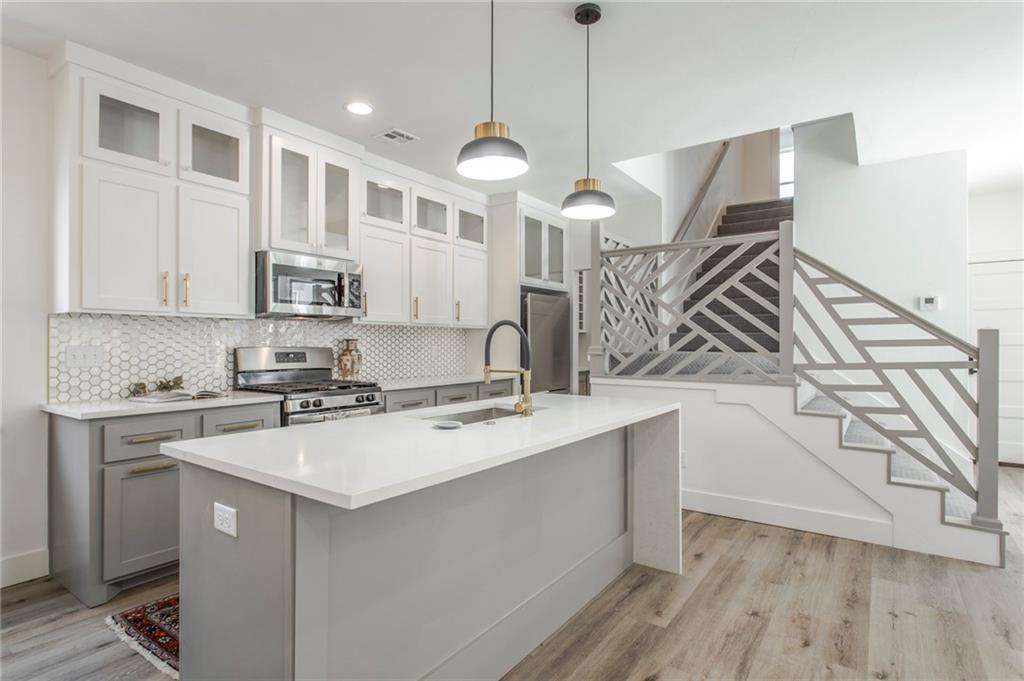 Modern kitchen with a large white island, hexagonal tile backsplash, and geometric metal staircase.