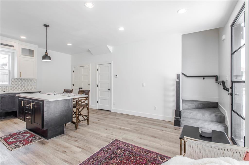 Open kitchen and dining area with a dark island, light wood floors, and carpeted stairs beside tall windows.