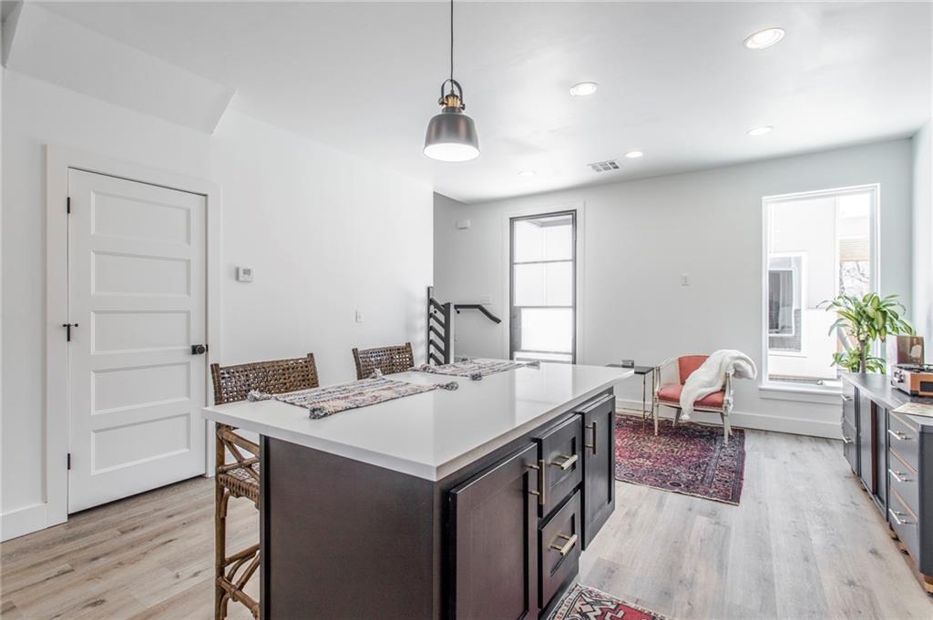 Bright kitchen with a large island, pendant light, and sitting area by tall windows.