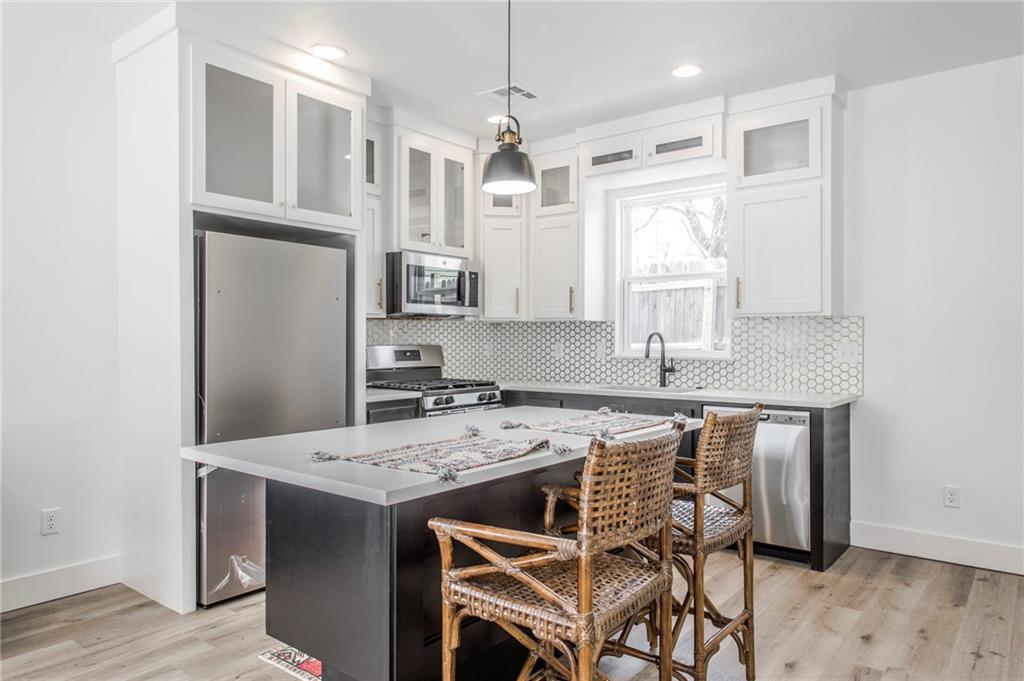 Modern kitchen with a dark island, white cabinets, hexagonal backsplash, and wicker stools.