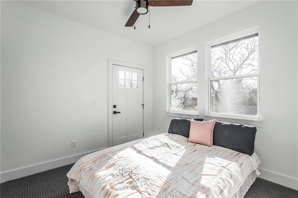 Bright bedroom with two large windows, a ceiling fan, and a bed with a pale quilt.