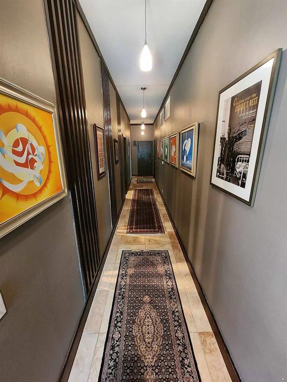 Narrow hallway with framed artwork, dark wood slats, and patterned rugs on a stone-tile floor.