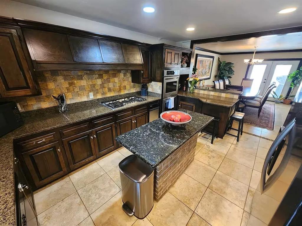 Kitchen with dark wood cabinetry, granite island, stone backsplash, and adjoining dining area.