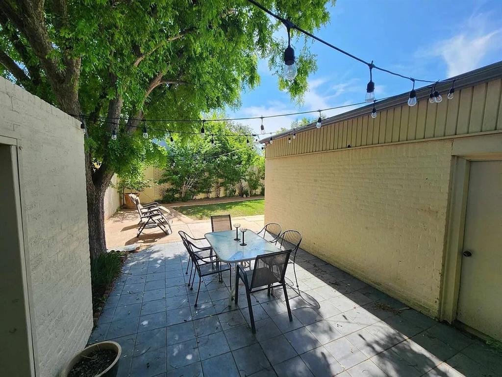 Tiled backyard patio with outdoor dining furniture, string lights, and a large shade tree.