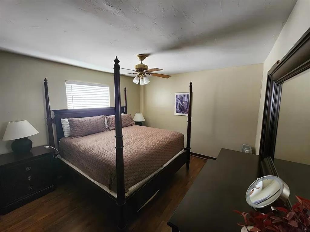 Bedroom with a dark four-poster bed, mauve bedding, hardwood floors, and a ceiling fan.