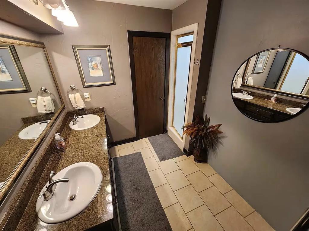 Bathroom with a granite double vanity, two sinks, and beige tiled floor.
