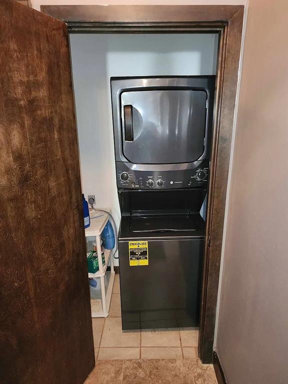 Laundry closet with a black stacked washer and dryer, tiled floor, and open wooden door.
