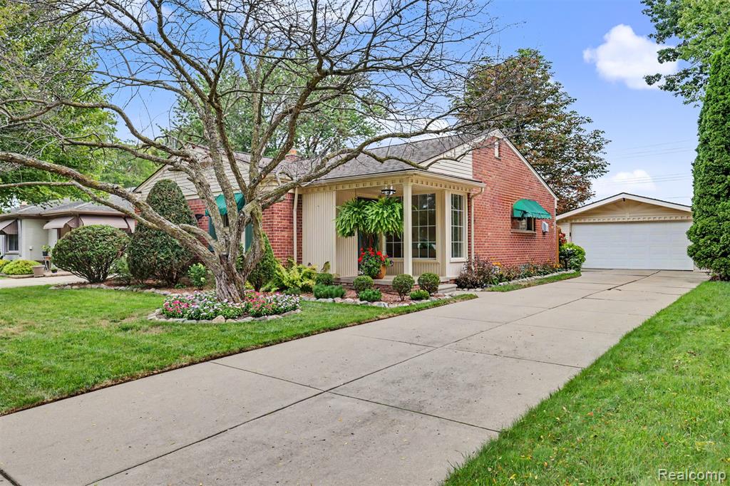 Red-brick house with a covered entry, landscaped yard, wide driveway, and detached garage.