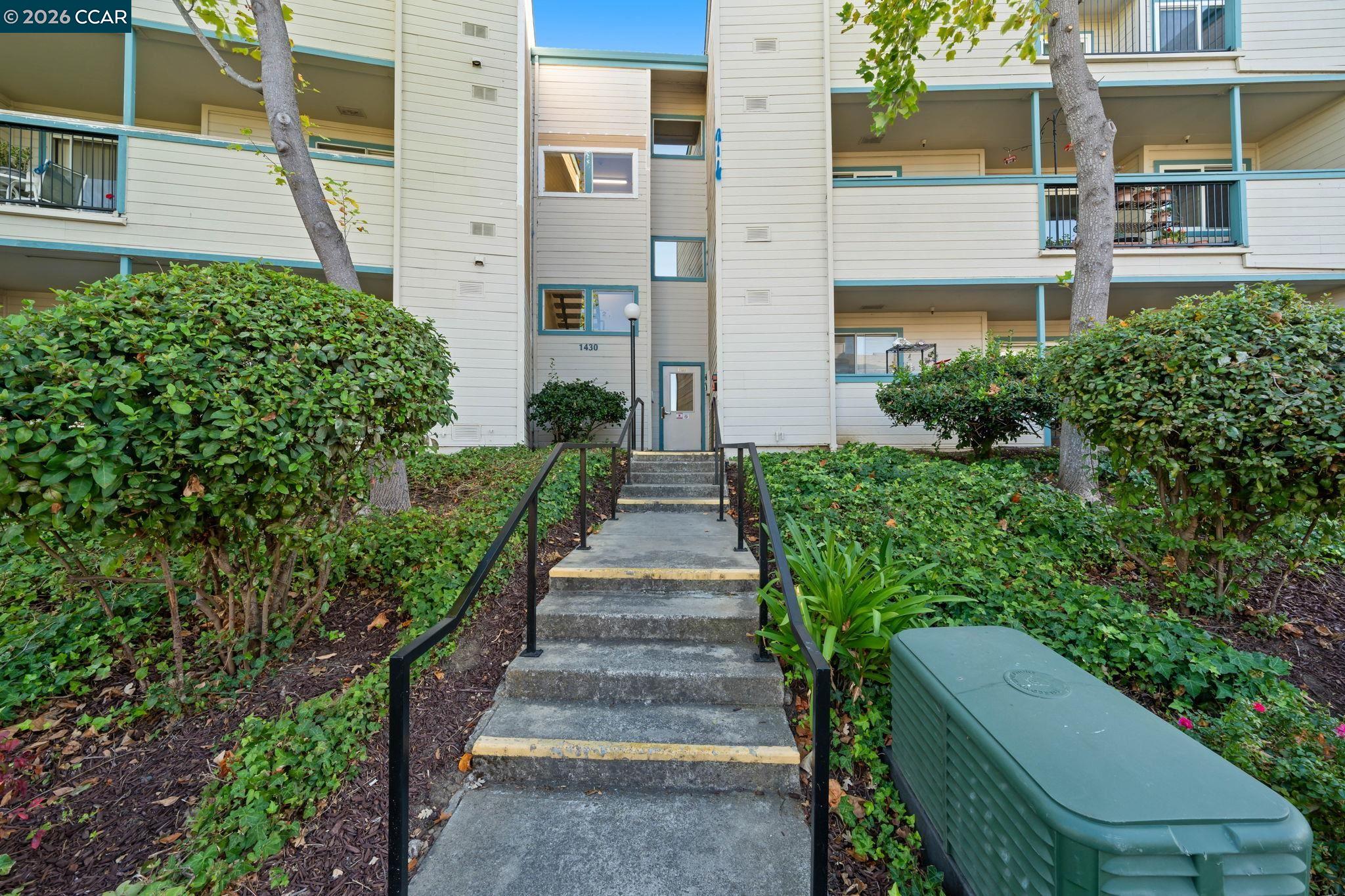 Condominium entrance marked 1430, reached by concrete steps and surrounded by shrubs and trees.