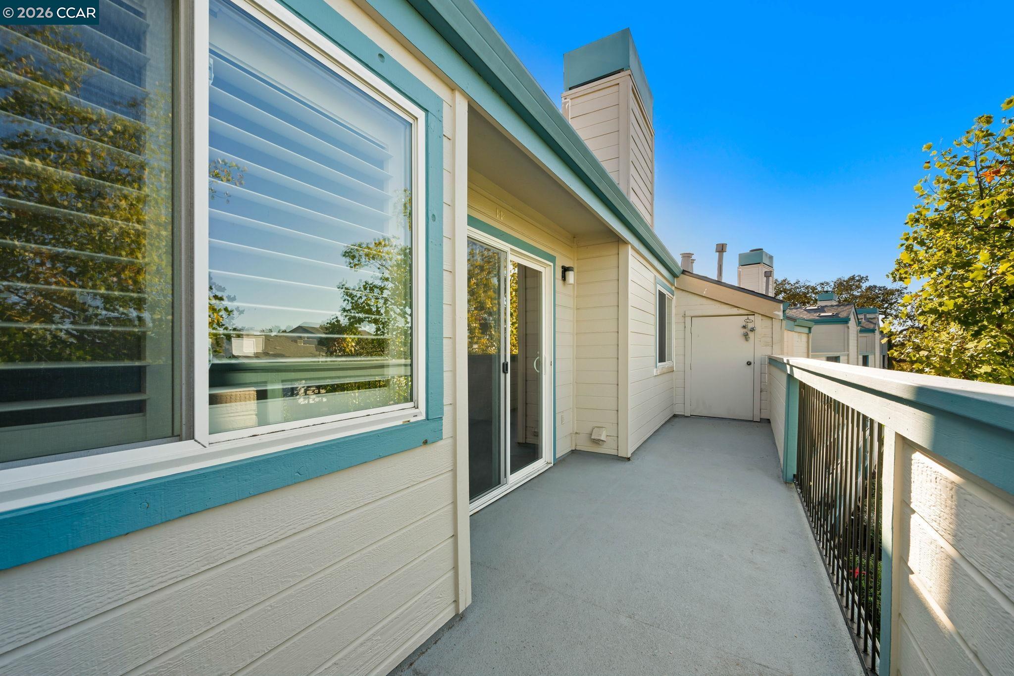 Condominium balcony with teal trim, sliding glass door, and black railing overlooking trees.