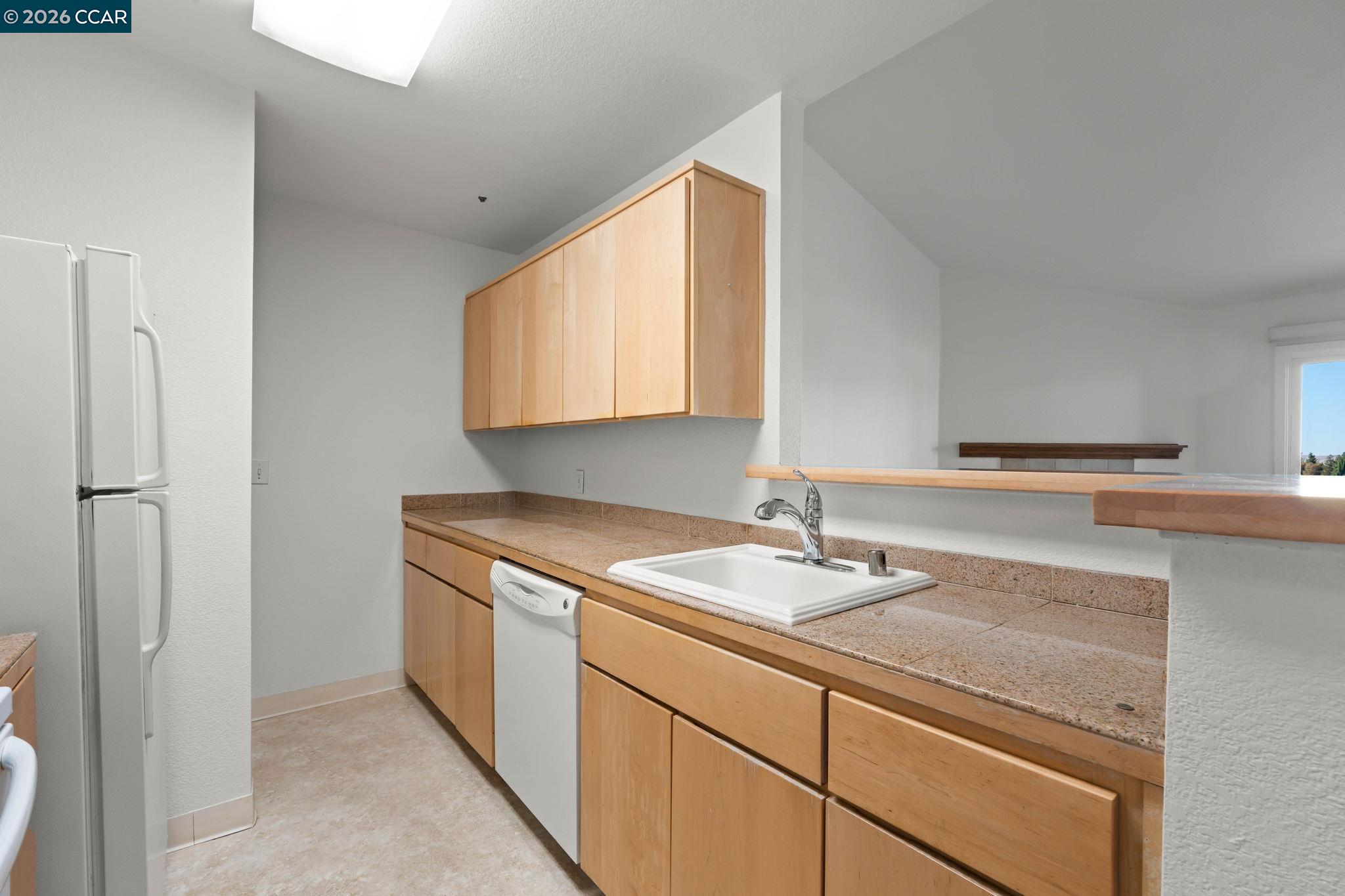 Kitchen with light wood cabinets, stone-look counters, a white sink, and a breakfast bar.