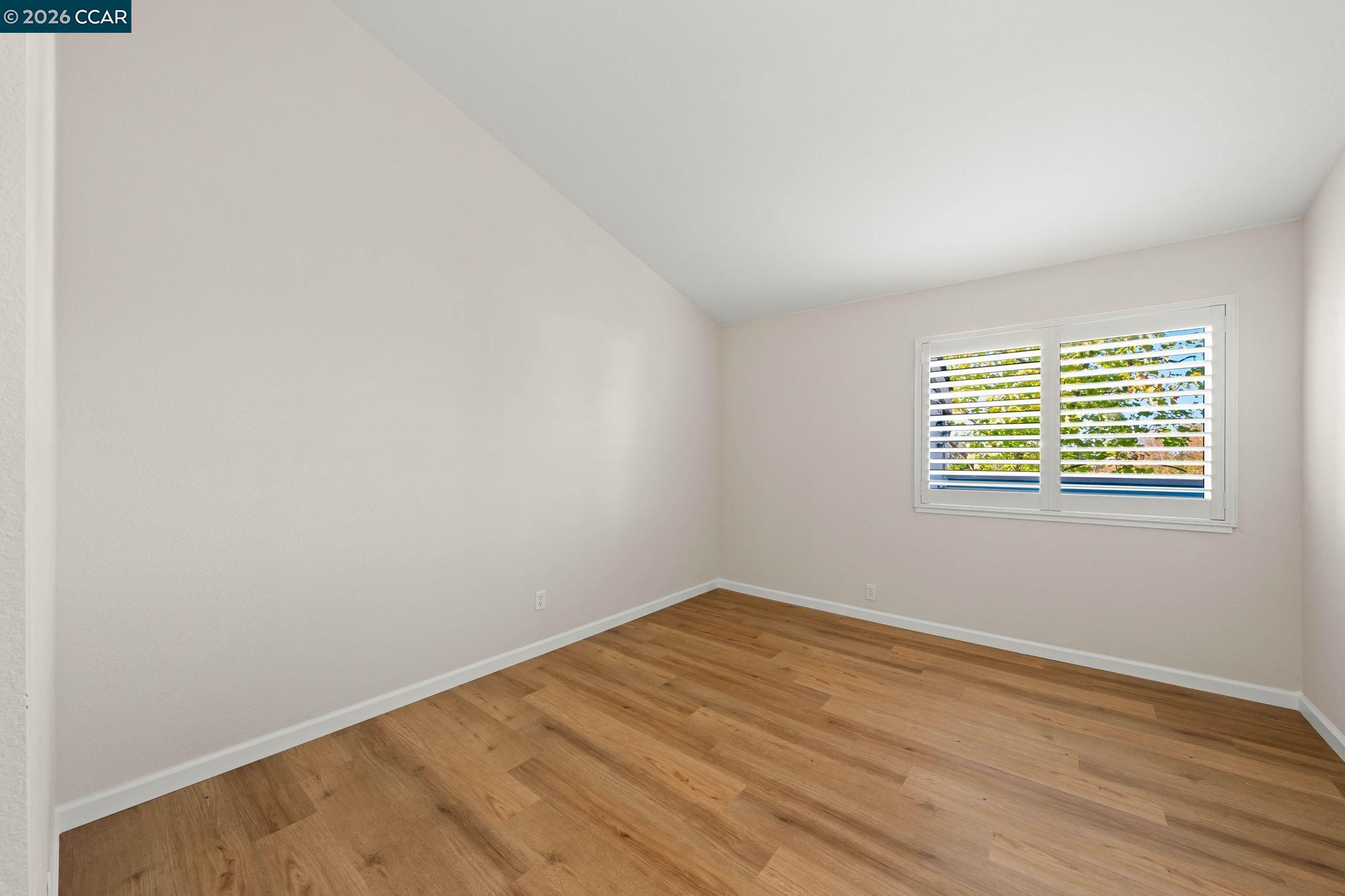 Empty bedroom with hardwood flooring and a shuttered window.