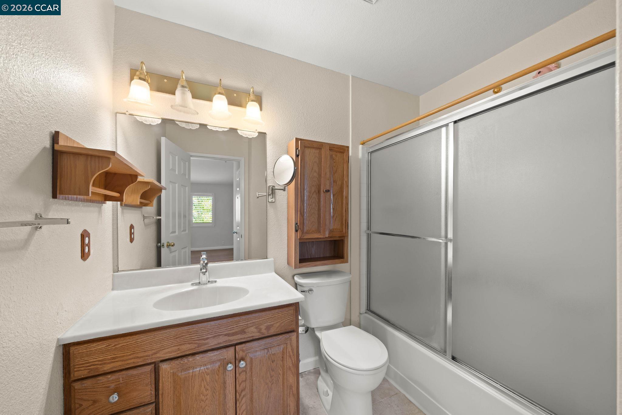 Bathroom with a wood vanity, mirrored medicine cabinet, toilet, and sliding shower doors.