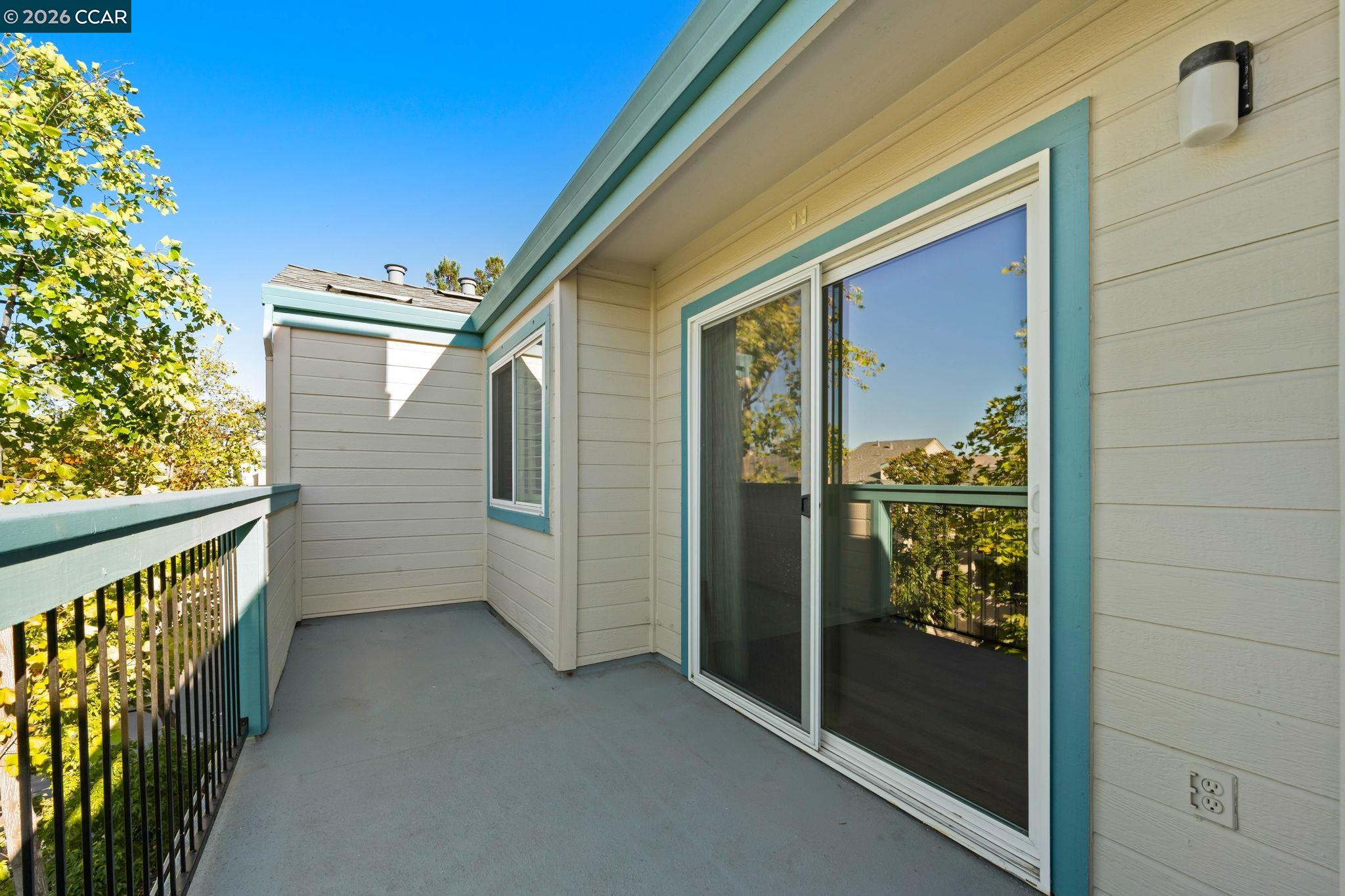 Private balcony with teal railings, a sliding glass door, and trees beyond.