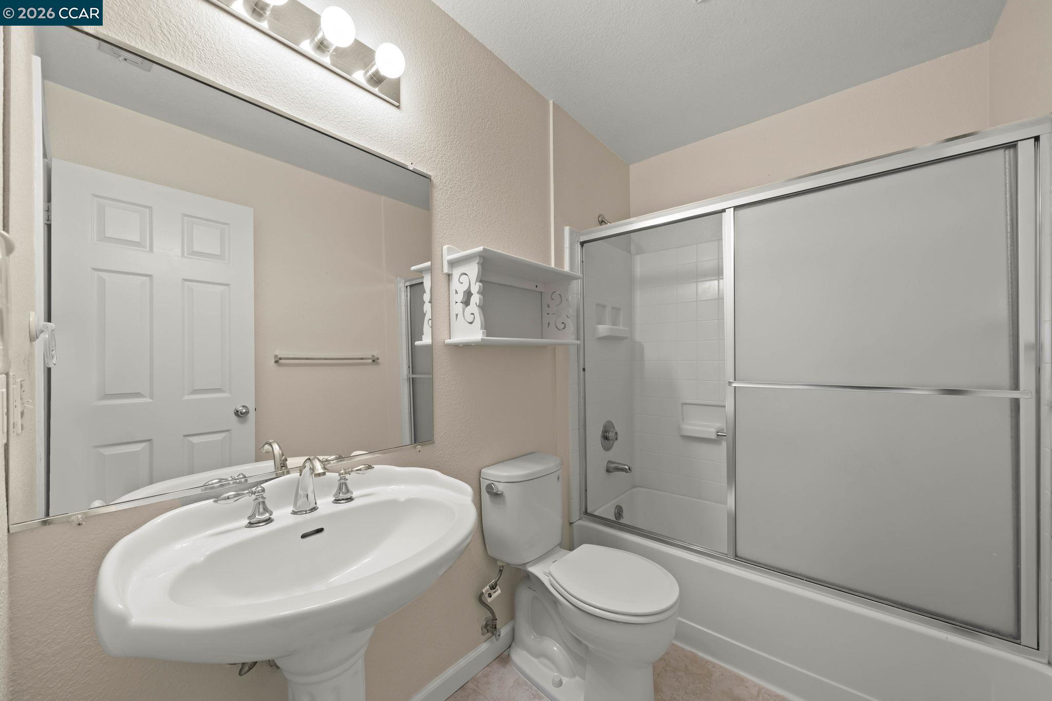 Bathroom with pedestal sink, mirrored wall, toilet, and tub with sliding glass doors.
