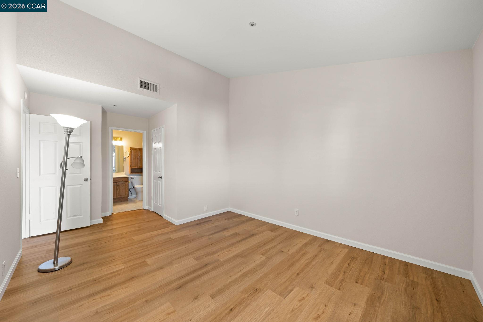 Empty room with light wood flooring and a doorway opening onto a bathroom.
