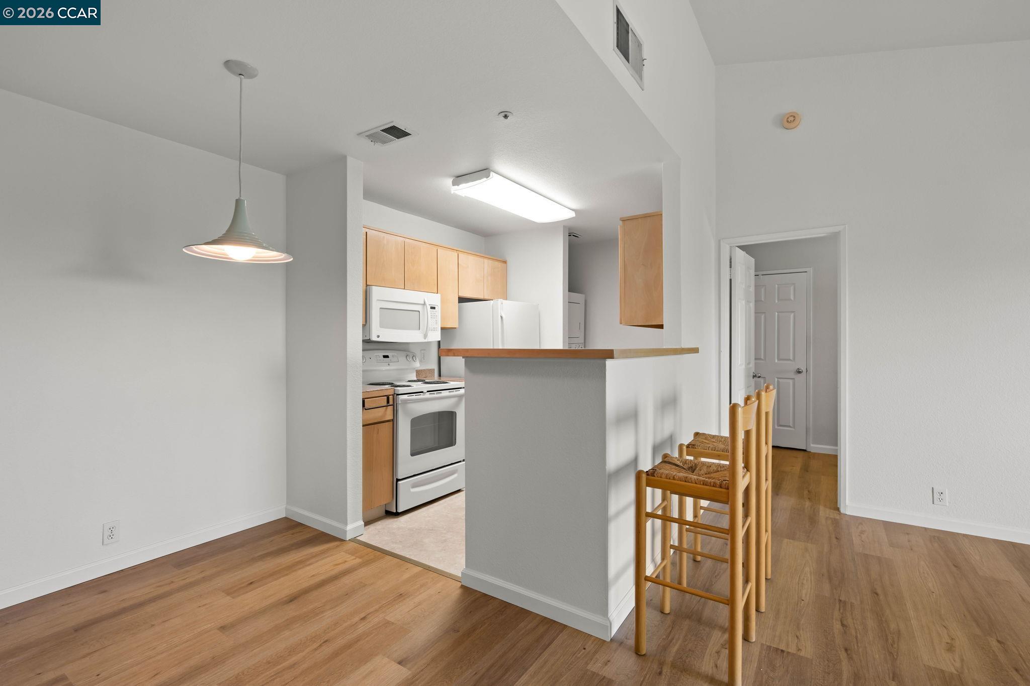 Kitchen and dining area with light wood cabinets, white appliances, and a breakfast bar with stools.