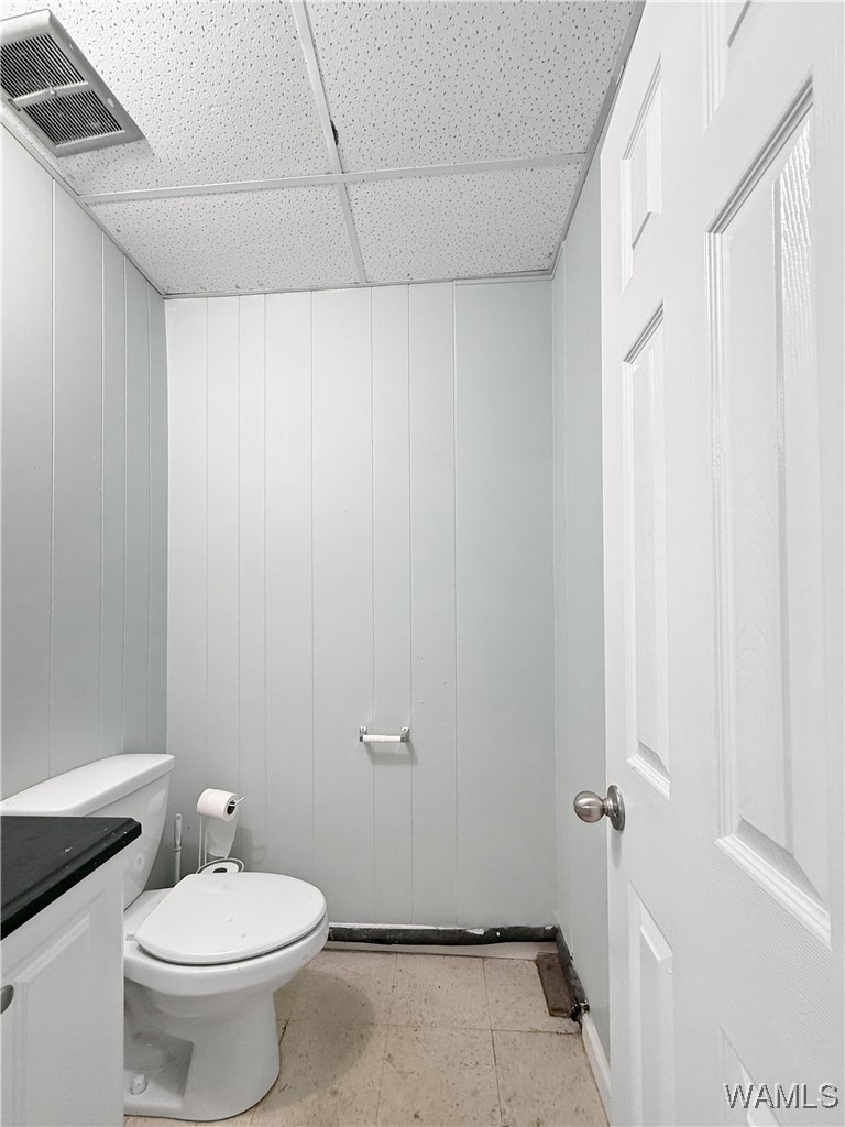 Small bathroom with a toilet, partially visible vanity, paneled walls, and tiled floor.