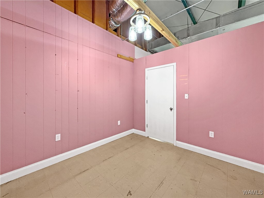 Empty retail suite with pink paneled walls, tan flooring, and an exposed ceiling.
