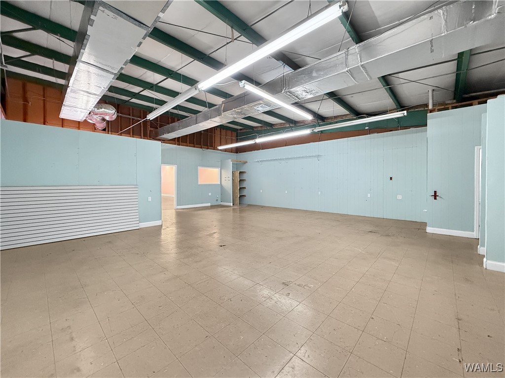 Vacant retail suite with pale blue walls, tiled floors, exposed ceiling ductwork, and a slatwall panel.