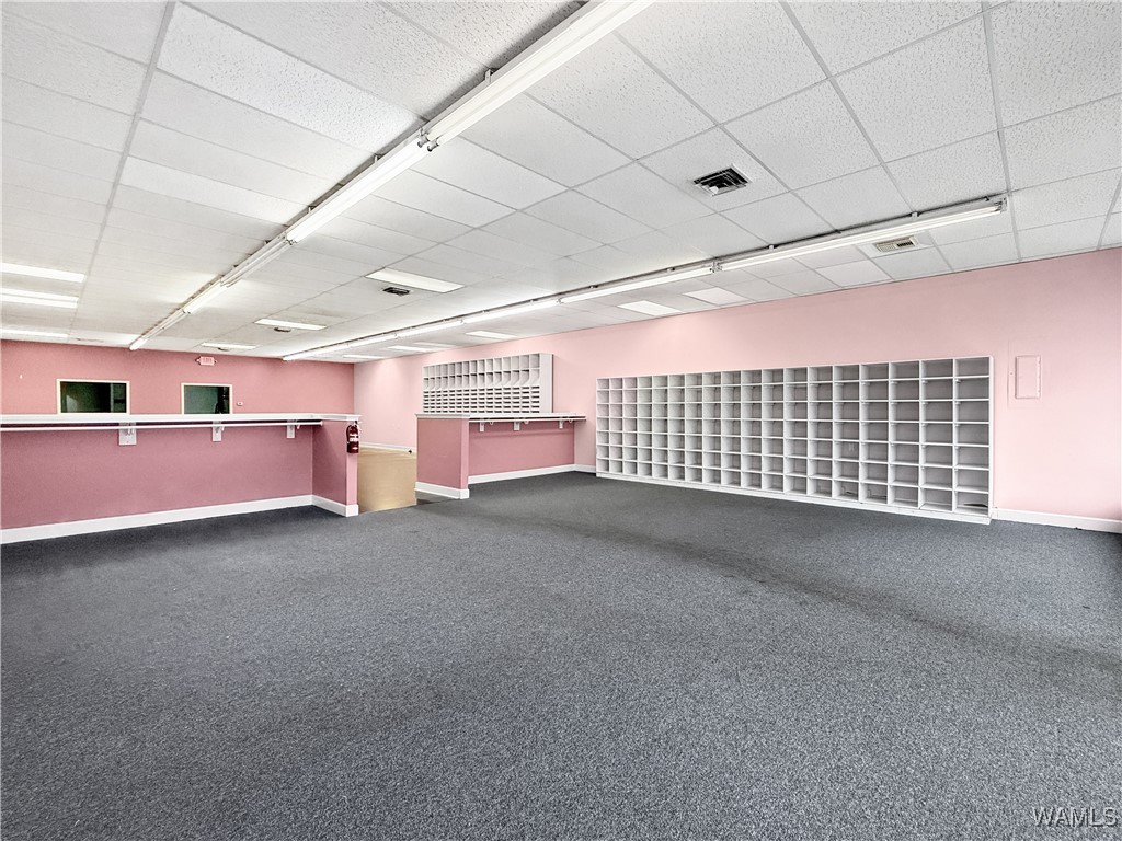 Vacant retail space with pink walls, gray carpet, white cubby shelving, and built-in counters.