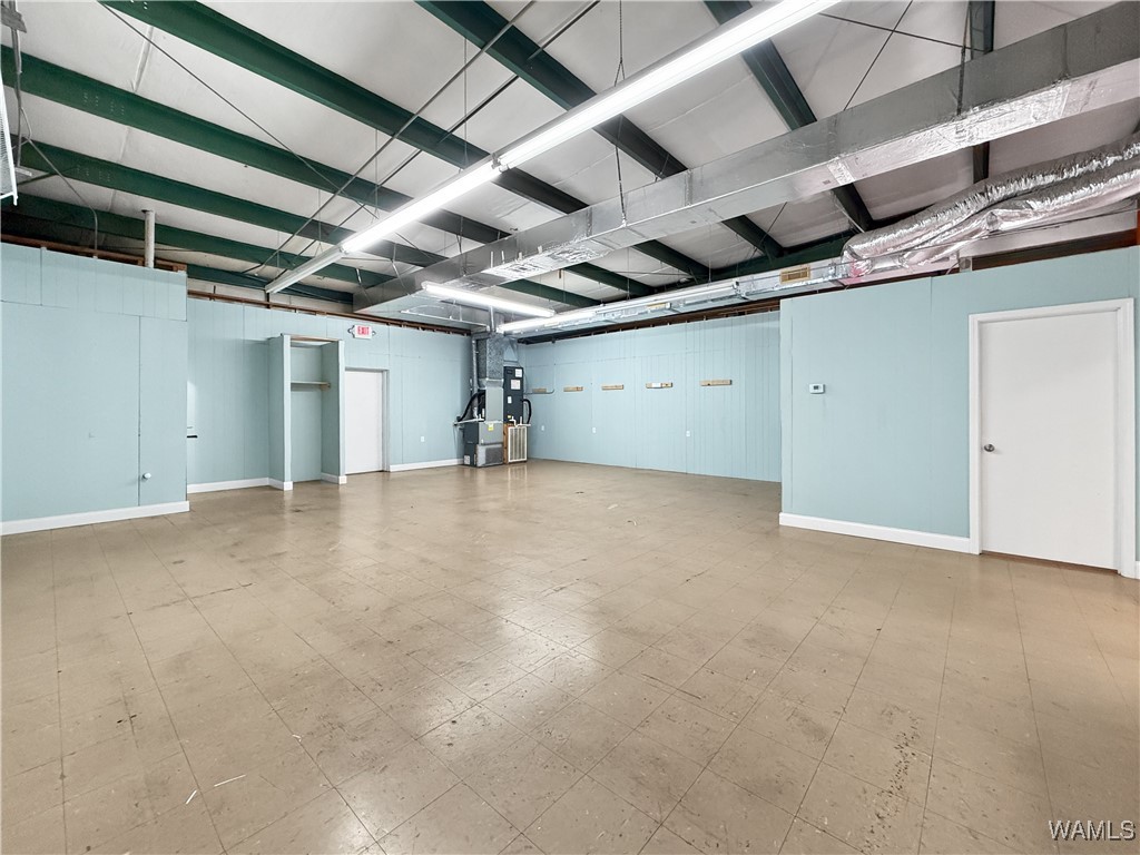 Vacant retail suite with pale blue walls, beige tile flooring, and exposed ceiling beams and ducts.