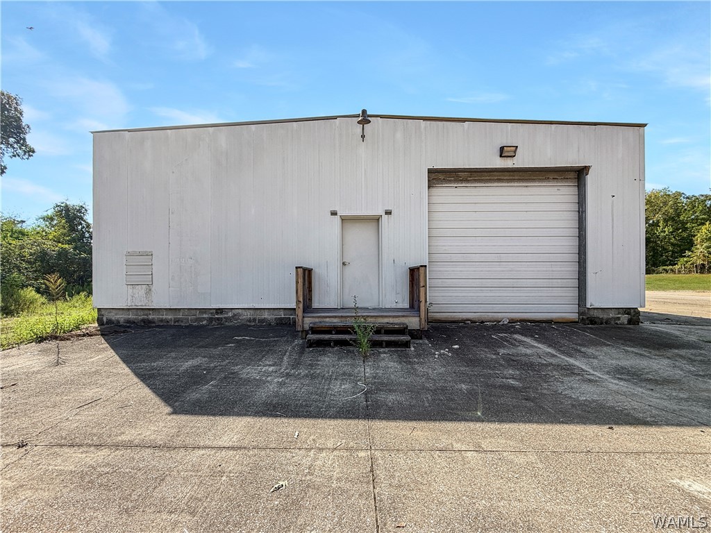 Metal warehouse with a large roll-up door, separate entrance, and broad concrete apron.