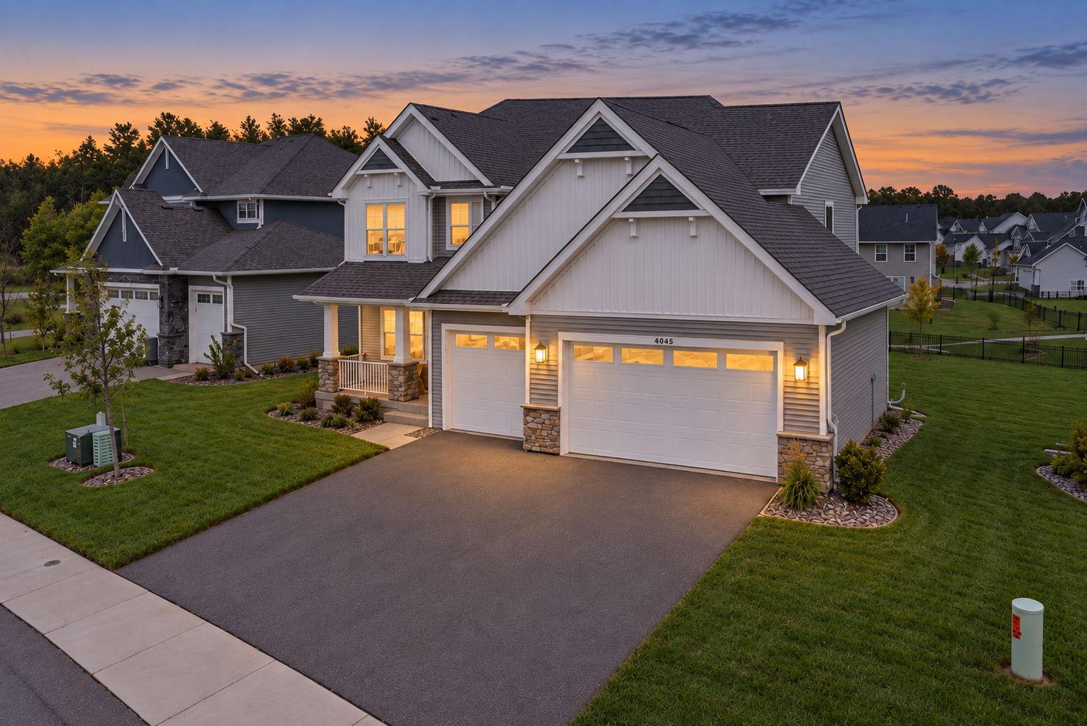 Two-story gray-and-white home with a double garage and glowing windows at dusk.