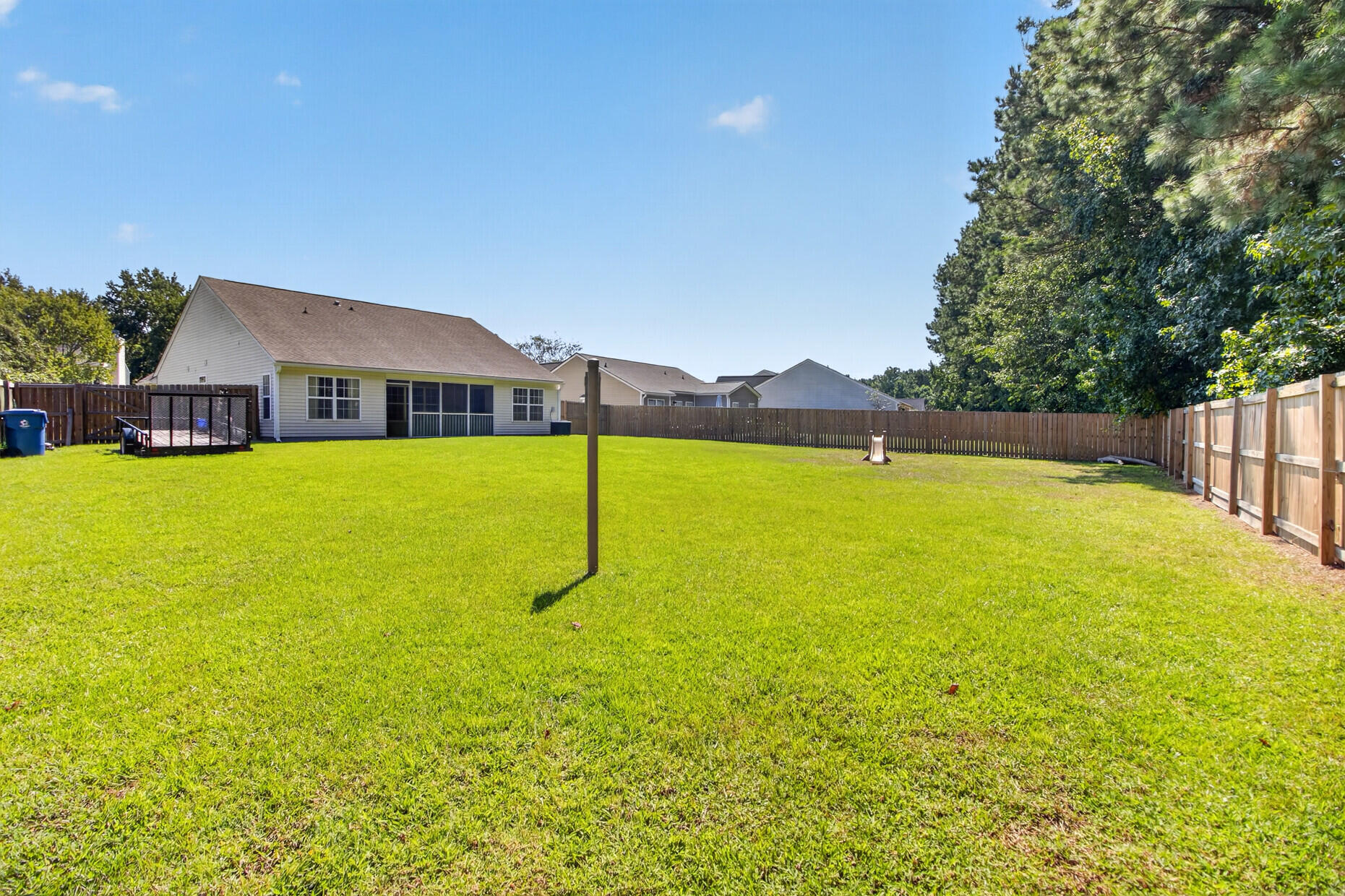 Fenced backyard with a broad green lawn behind a house, viewed on a sunny day.
